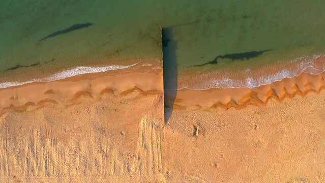 Aerial view of a narrow dock on a sandy beach