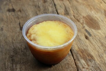 Closeup shot of homemade orange and yellow pudding in a plastic container on wooden background
