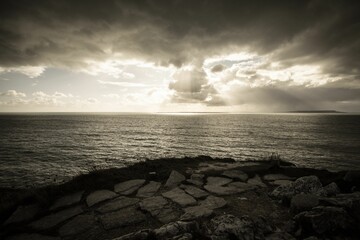 Black and white shot of a beautiful seascape with sunrays coming out of the clouds - Powered by Adobe