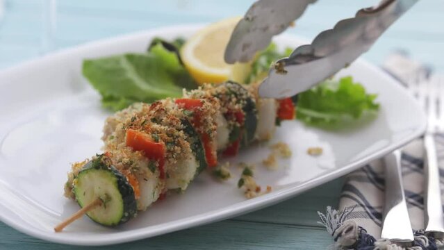 Fish and vegetable skewers that are placed on a platter decorated with lemon and salad