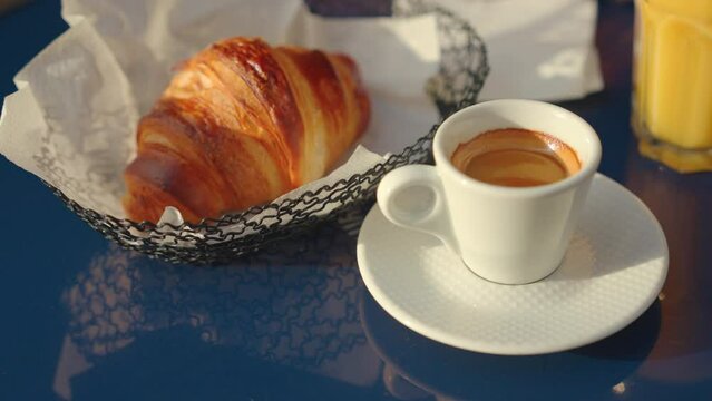 White cup with coffee and croissant on a blue table in a cafe