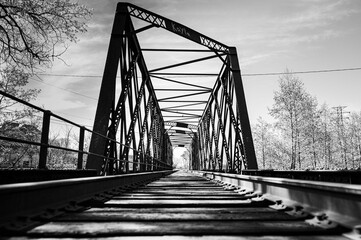 Black and white of railroad bridge, low angle in Wisconsin with snowy trees