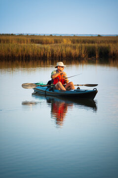 Surrounded by marsh grass, an older man fishes from a kayak in Bayou Thunder Von Tranc, Louisiana