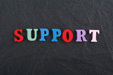 SUPPORT word on black board background composed from colorful abc alphabet block wooden letters, copy space for ad text. Learning english concept.