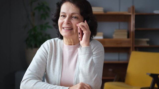 Happy middle aged senior woman talking on smartphone with family friends. Older mature lady with cell phone chatting with grown up children, resting in at home. Older generation modern tech usage