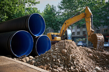 Large plastic corrugated pipes for water supply lie on the street in the city. - obrazy, fototapety, plakaty