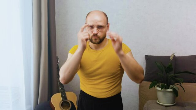 A bald, funny, nerdy man puts on glasses, crosses his arms over his chest and looks too seriously at the camera. An abstruse intellectual with a high IQ