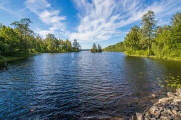 Beautiful view of green trees around the shiny blue lake under cloudy blue sky