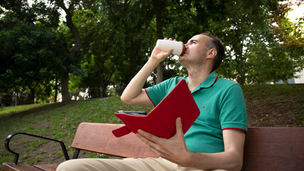 Naklejka premium man sitting on a bench drinking coffee with an e-book in his hand