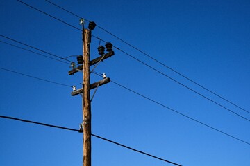 Low angle shot of a electric pole with wires on a background of blue sky