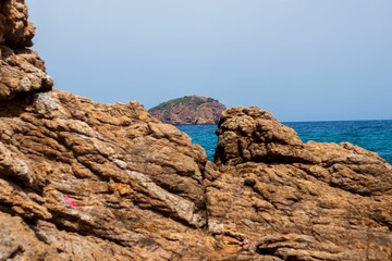 Illuminated stone formation by sunlight on a sunny day, with an island in the sea in the background