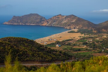 Aerial view of a beach and people enjoying a sunny day, with a forested mountain in the background