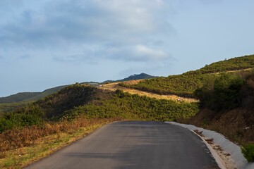 Mountain road, leading through beautiful green hills, on a sunny day, with clouds on the sky