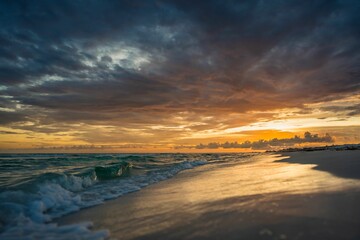 Fototapeta na wymiar Dramatic sunset over the sea waves washing the sandy beach