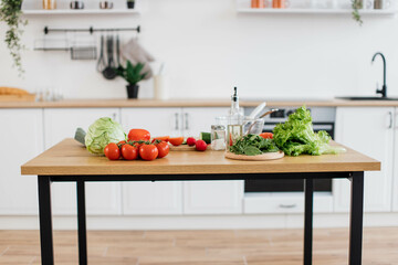 Wooden table filled with red and green organic components of healthy balanced diet on kitchen background. Common raw vegetables and greens for delicious homemade breakfast being ready for cooking.