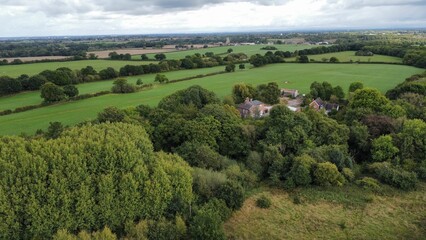 Aerial of small houses surrounded by green trees and fields in England under the cloudy sky