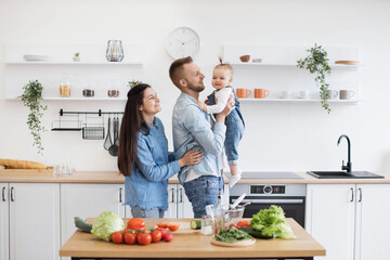Adorable little lady in denim clothes laughing with caring parents while dad holding baby daughter...