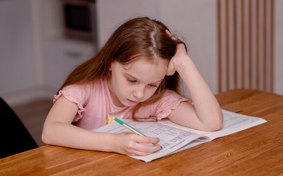 The girl sits at the table and solves problems, does her homework. School theme, vacation assignments