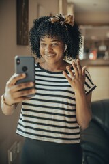 Vertical shot of a young woman on a video call using  smartphone and wearing wireless earbuds