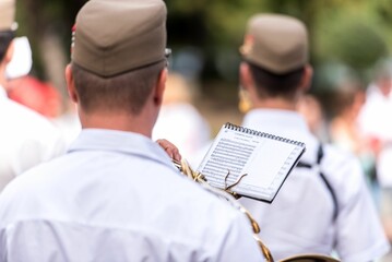 Brass band musicians holding sheet music from behind in a park