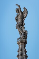 Fototapeta na wymiar Vertical shot of the statue of angel on roof of Milan Cathedral, Italy on a blue sky background