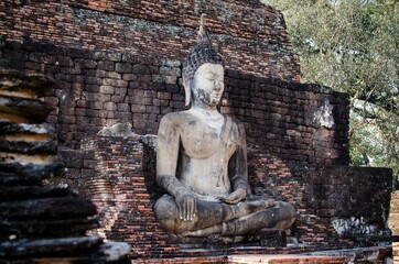 Fototapeta premium Sitting Buddha in Sukhothai, Thailand against a crumbled brick structure