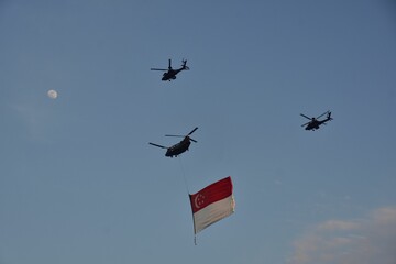 Helicopters flying in the blue sky while holding the Singapore flag