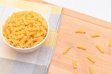 Uncooked Fusilli Pasta in White Bowl on Wooden Board. Raw and Dry Macaroni. Unhealthy and Fat Food. Italian Culture