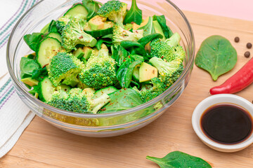 Fresh Green Salad of Avocado, Broccoli, Spinach and Cucumber with Soy Sauce and Red Hot Pepper on Wooden Cutting Board. Vegan Salad. Vegetarian Culture. Raw Food. Healthy Eating and Vegetable Diet