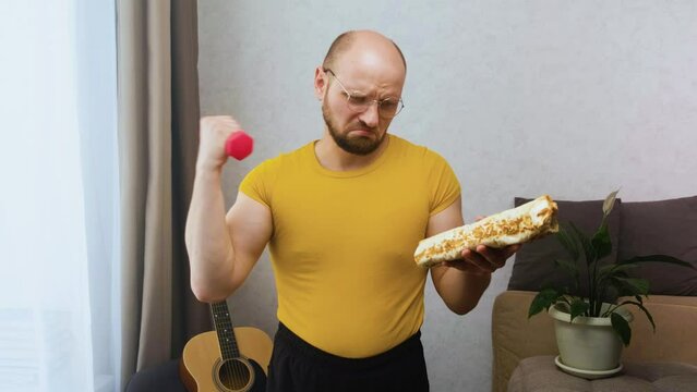 Muscular man trains and looks sad at calorie food. Diet and willpower during fat burning. Temptation by food during weight loss