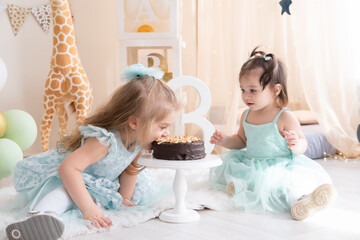 Two little girls in blue dresses eating chocolate birthday cake