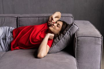 Obraz premium Young woman sitting on couch at house. Female stretching body after wake up on sofa