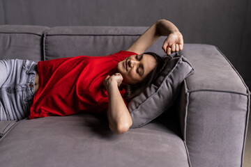 Young woman sitting on couch at house. Female stretching body after wake up on sofa