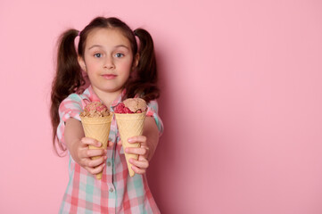 Detail on waffle cones with delicious ice cream in the hands of a cute baby girl, holding out at camera refreshing sweet frozen dessert, isolated on pink background with copy ad space. Summer concept