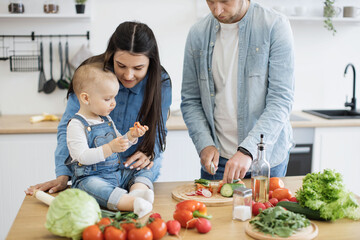 Sweet little girl in denim wear holding small slice of red vegetable while caring mother describing new product. Mother and daughter getting to know more about texture and color of hard food.