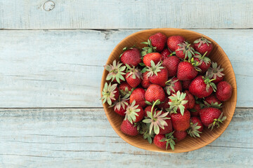 Top view of wooden bowl full of freshly picked ripe red strawberries on the rustic wooden background. Flat lay. Fresh organic food full of vitamins. Dieting concept
