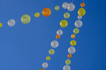 Low angle shot of white and yellow paper lanterns on a wire against a cloudless blue sky