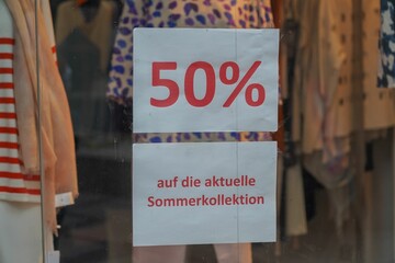 Sign with the inscription "50 percent off the summer collection" in the window of a clothing store