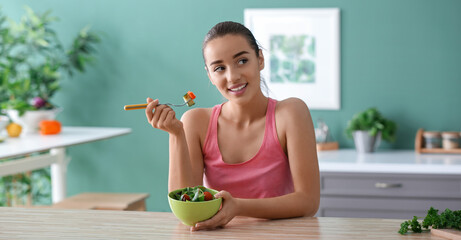 Young woman eating vegetable salad in kitchen