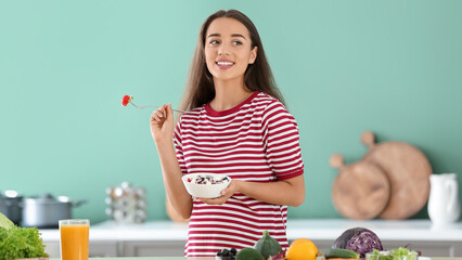 Young pregnant woman eating vegetable salad in kitchen