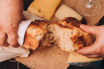 Man tearing the freshly baked Italian bread with cheese and a glass of wine on the table