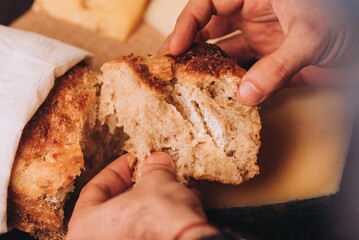 Closeup of a man tearing the freshly baked Italian bread on the blurred background