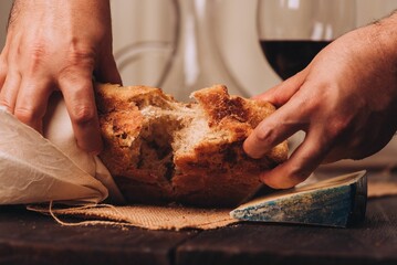 Man tearing the freshly baked Italian bread with cheese and a glass of wine on the table