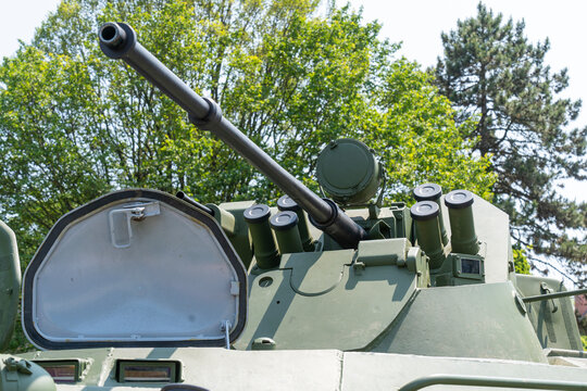 The turret of a green armored personnel carrier equipped with a heavy machine gun and fog grenade launcher