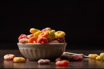 there is a bowl of fruit cereal on a table and a spoon sitting next to