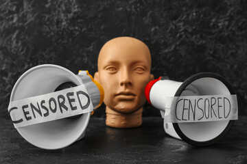 Taped megaphones with word CENSORED and human head on dark table
