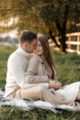 Fototapeta premium Mothers day. Stylish marriage pregnant couple waiting for baby. Man hugs and touches woman belly outdoors on plaid on grass. Family day. Pregnancy, parenthood, motherhood, love, family concept.