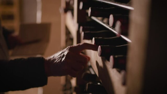 Closeup of a man with a jacket straightening the old wine bottles in the wine cellar