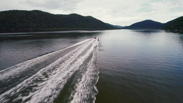Drone shot over a boat driving in Hawkesbury River with green hills with cloudy sky in Australia