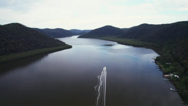 Aerial shot over a boat driving in Hawkesbury  River with green hills with sunset sky in Australia